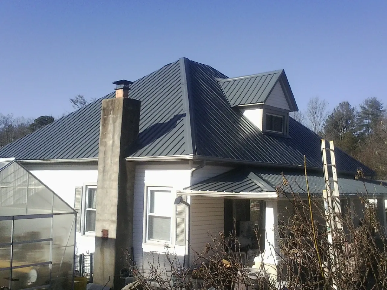 Dark blue standing seam metal roof on a white farmhouse with dormer — Slate & Tile Roof Repair by Roofing Brothers in Lake Panasoffkee