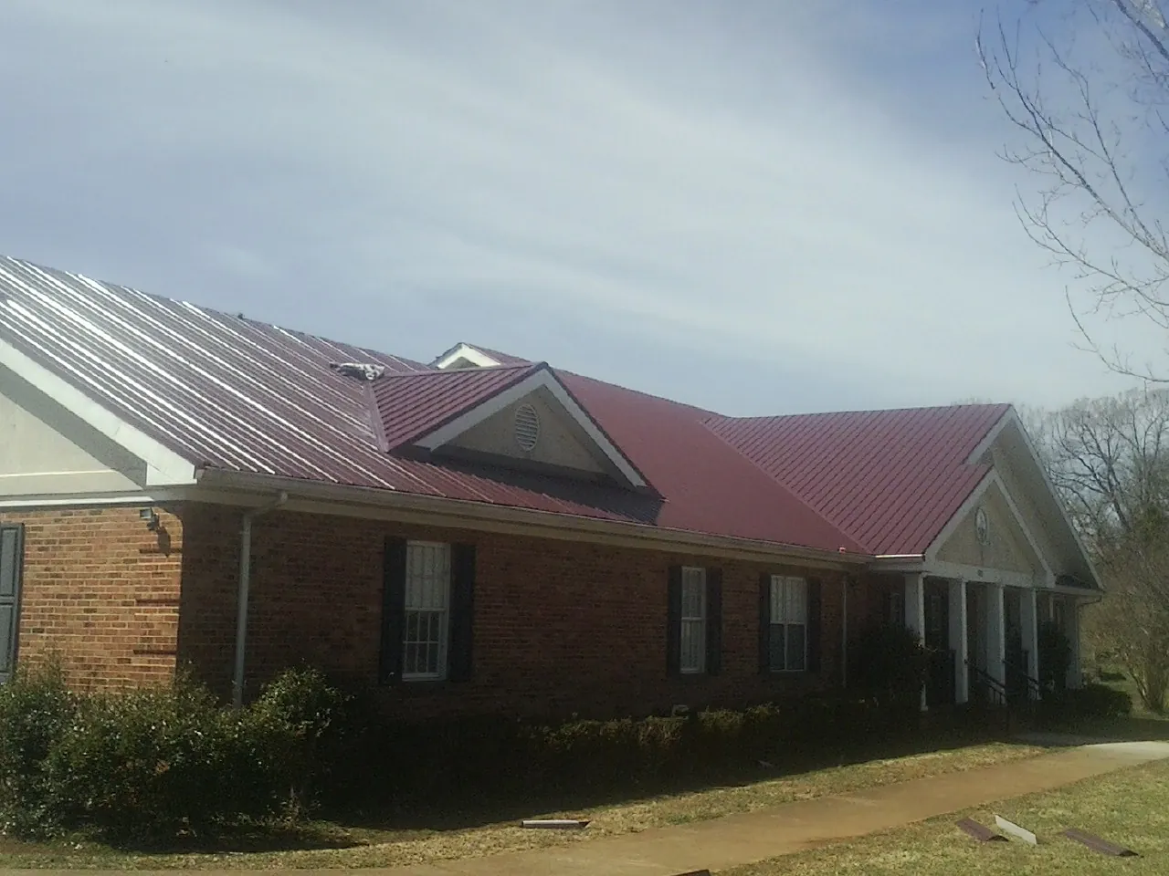 Red metal roof with gabled entries on a long brick building, from a Hail Damage Roof Repair job in Lake Panasoffkee