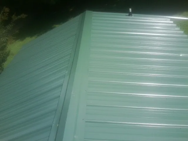 New green metal panels meeting at the ridge of a roof — Flat Roof Repair work by our crew in Lake Panasoffkee