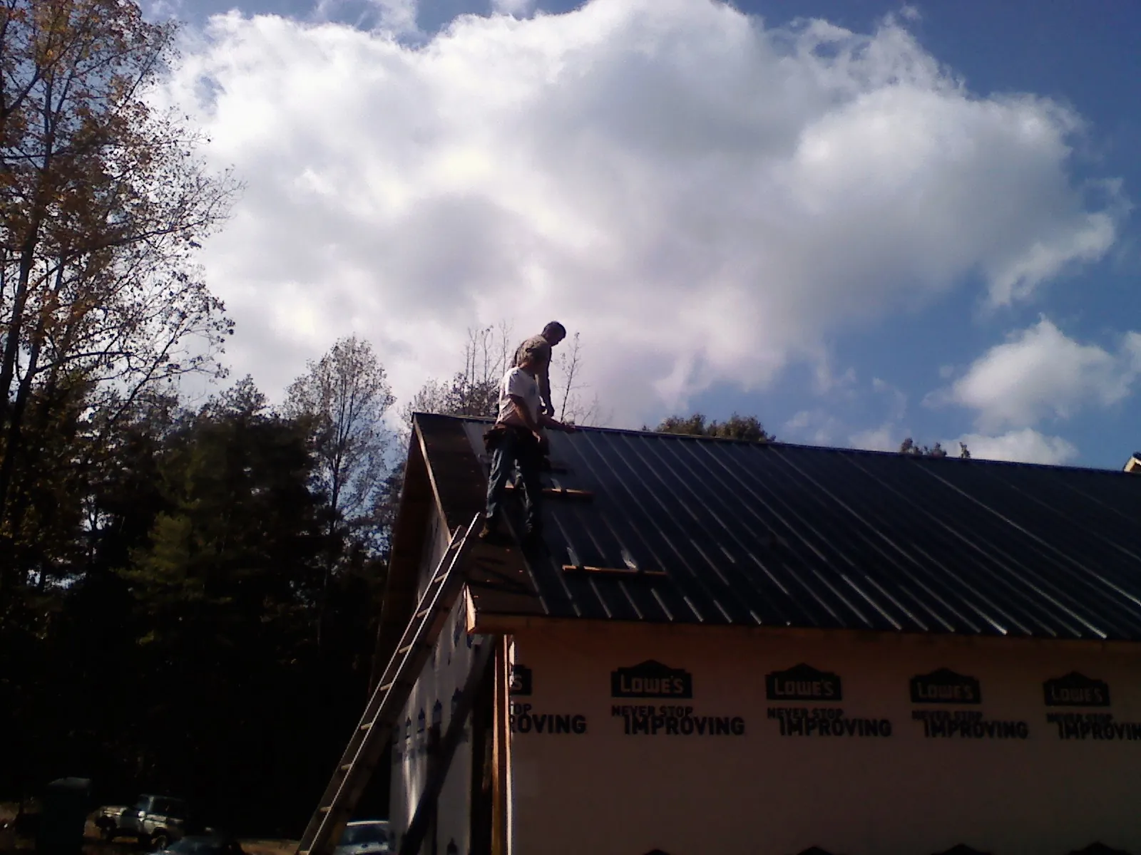 Roofer fastening dark metal panels high against a cloudy sky, from a Roof Inspection job in Lake Panasoffkee