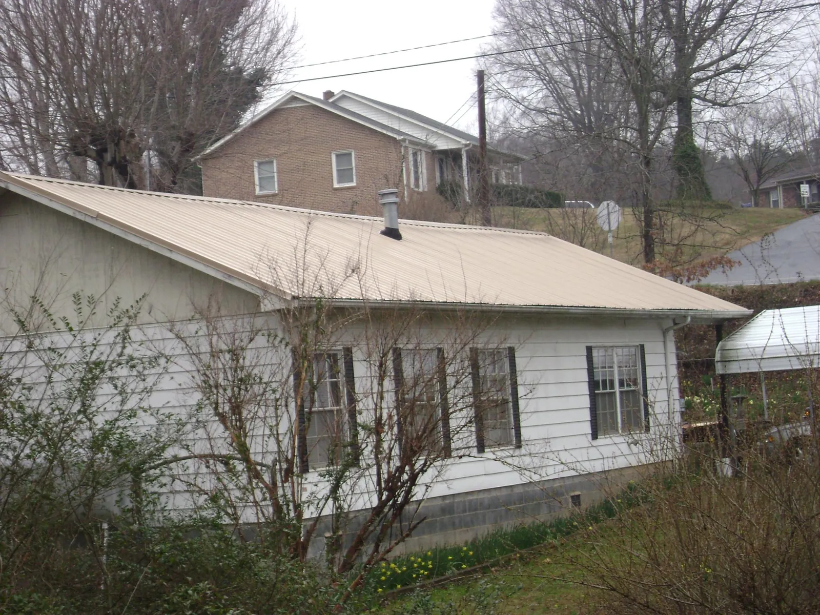 Tan metal roof on a white sided house set into a hillside — Commercial Roofing by Roofing Brothers in Lake Panasoffkee