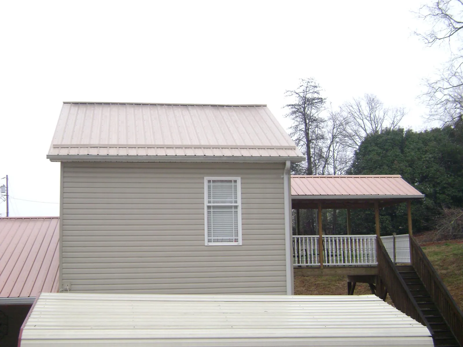 Tan metal roofs on a two story addition and attached porch, from a Roof Replacement job in Lake Panasoffkee